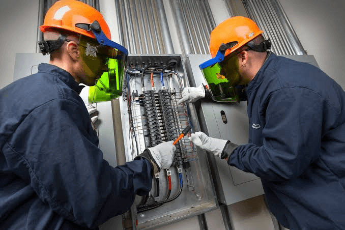 Certified electrician inspecting electrical panel with safety gear